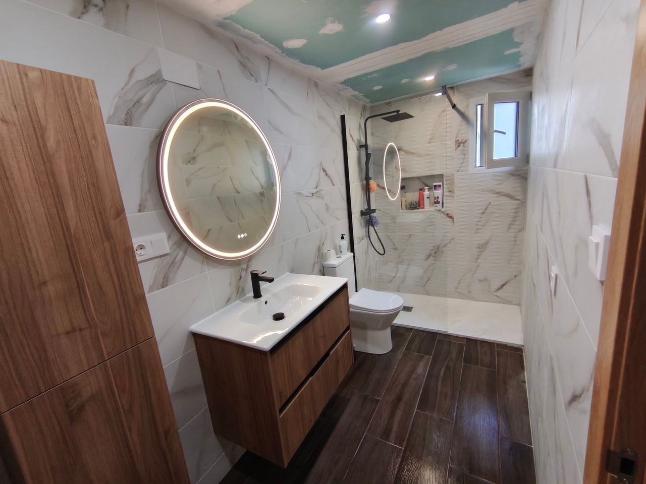 Reforma de baño con mueble de madera y espejo redondo en Albacete, realizada por DCELITE